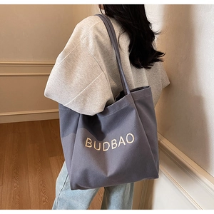 Detail of purple canvas tote bag with BUDBAO embroidery worn by a model in interior setting