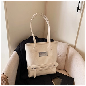 Close-up of beige PU leather tote bag with metallic logo and zipper detail on sofa