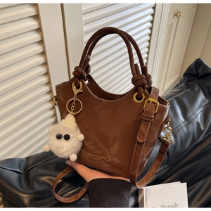 Detail einer braunen PU-Leder Eimertasche mit Tragegriffen und weißem Plüsch-Charm-Anhänger