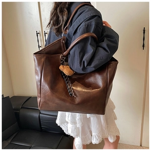 Detail of dark brown leather tote bag with plush bear charm and woven tassel accent