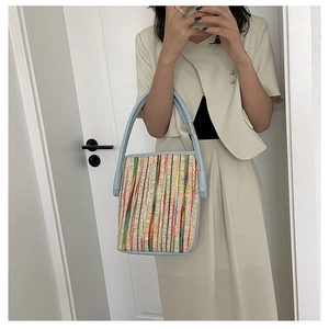 Detailed texture of multi-color woven stripes on natural straw bucket bag with blue leather strap