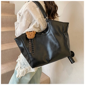 Close-up of black PU leather tote bag featuring a cute brown plush bear charm detail
