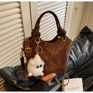 Detailansicht der glänzenden braunen Beuteltasche mit Plüsch-Anhänger und Gold-Details
