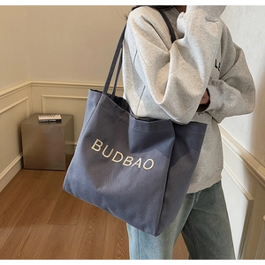 Detail of blue canvas tote bag featuring embroidered BUDBAO lettering and sturdy shoulder straps