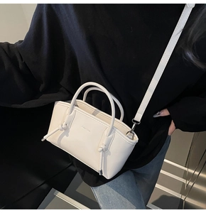 Dettaglio borsa crema con nodi intrecciati sui manici e logo impresso sulla superficie
