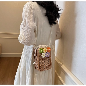 Détail du sac seau en paille avec fleurs en tricot et bandoulière en perles nacrées