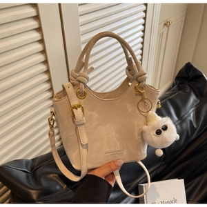 Detail der beigen Beuteltasche mit Knotengriff, Goldbeschlägen und Plüschanhänger