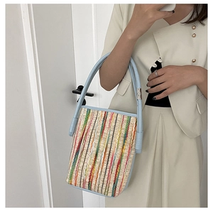 Detail view of woven bucket bag with colorful stripes and light blue leather handles