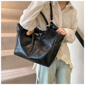 Detailed view of black PU leather tote bag featuring a plush ball and tassel charm
