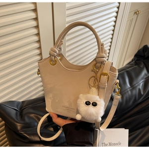 Detailansicht der cremefarbenen PU-Leder-Beuteltasche mit Goldbeschlag und Plüsch-Anhänger