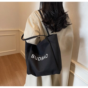 Side view of large black canvas tote bag with BUDBAO logo styled on a beige trench coat