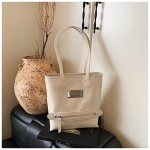 Close-up of cream white tote bag featuring distressed leather texture and front zip pocket