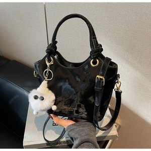 Detail der schwarzen glänzenden Beuteltasche mit goldenen Ringen und Plüsch-Anhänger
