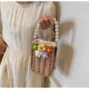 Détail du sac seau en paille tressée avec fleurs en tricot et poignée en perles