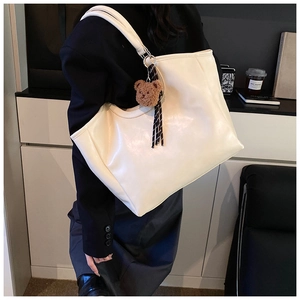 Side view of cream oversized tote bag with plush bear charm and checkered ribbon