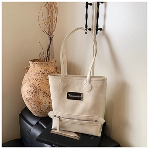 Detailed macro view of cream-colored pleated faux leather tote with silver brand plaque