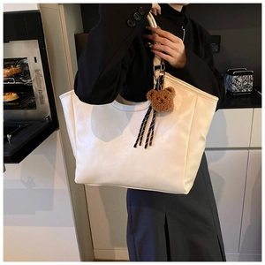 White leather tote bag with brown bear charm and striped cord detail on shoulder strap