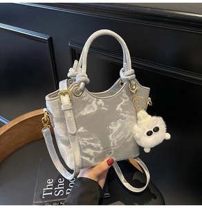 Detailsicht der silbernen Marmor-Eimertasche mit flauschigem Anhänger und Goldbeschlägen