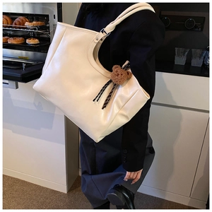 Detail of cream white tote bag with bear charm worn over shoulder in a cozy cafe