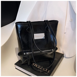 Detail of silver brand plate and zipper on glossy black oil-wax leather tote bag