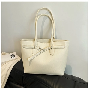 Gros plan d'un sac cabas crème avec texture grainée et boucle décorative sur canapé
