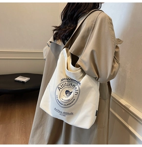 Vue latérale d'un grand sac cabas en toile blanche avec emblème noir porté par un mannequin