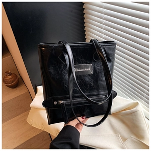 Close-up of black oily waxed leather tote bag featuring a metallic logo plate and glossy texture