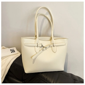 Détail du sac cabas en cuir crème à texture litchi sur un canapé en cuir noir avec revue