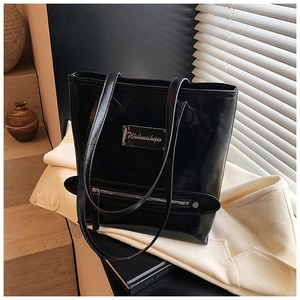 Détail d'un grand sac cabas en cuir verni noir avec texture brillante et plaque en métal