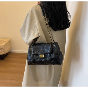 Close-up of black quilted leather chain bag with gold hardware worn by a model