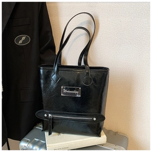Close-up of black glossy crinkled tote bag with silver logo plaque and decorative zipper