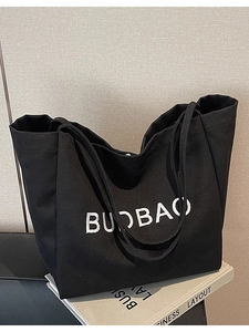 Black canvas tote bag with BUOBAO embroidery and snap closure on a pile of books