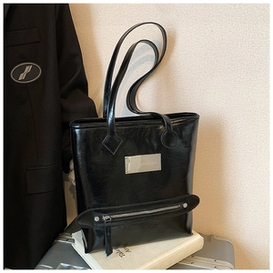 Close-up of black glossy tote bag showing textured patent leather and silver metal plaque