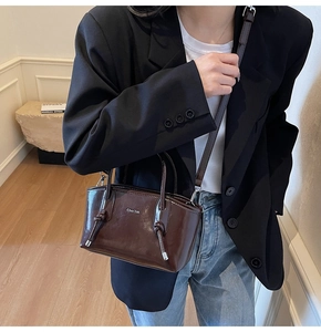 Dettaglio borsa in pelle lucida marrone con decorazione nodo e tracolla sottile