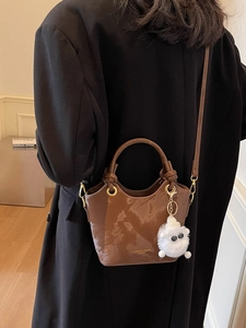 Braune Lackleder-Eimertasche mit Tragegriff und Plüsch-Anhänger am Modell gezeigt