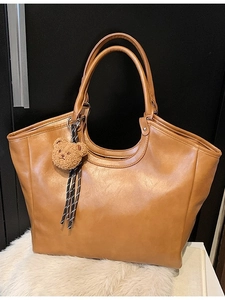 Brown faux leather tote bag with dual handles and teddy bear charm on white fur rug