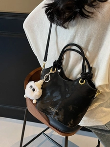 Modische schwarze Leder Eimertasche mit goldenen Details und weißem Plüsch-Anhänger