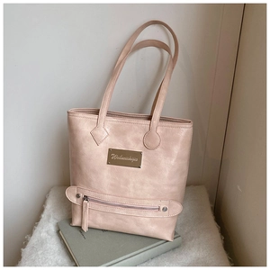 Détail du cabas rose clair avec texture litchi et logo doré sur un livre vert