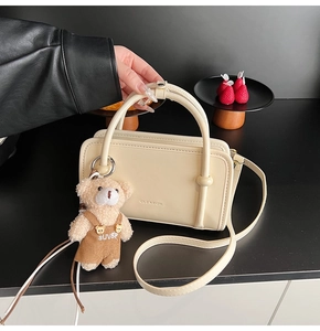 Detail of beige square crossbody bag with plush bear charm and embossed logo