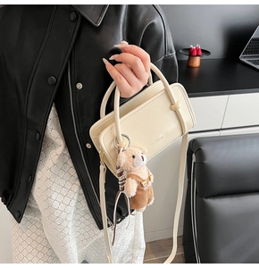 Detail of cream rectangle handbag with round handles and cute plush bear charm