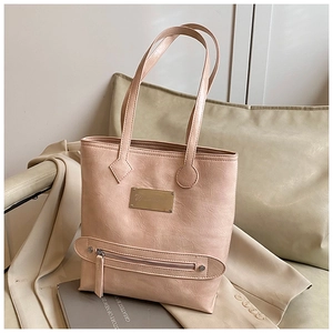 Detailed view of the gold metal logo plate and zip accent on a beige faux leather tote bag