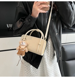 Detail of cream white rectangular leather handbag with a plush bear charm and thin strap