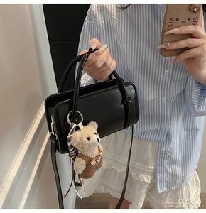 Mirror selfie showing a black leather handbag with a plush bear charm and long strap