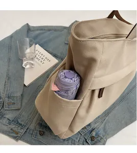 Detail of beige canvas tote with side pocket holding a purple umbrella and zipper closure