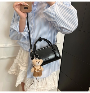 Detail of black crossbody bag featuring a cute teddy bear charm and sleek metal logo