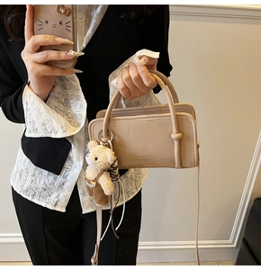 Detail of beige structured handbag with round handles and a cute plush bear charm accessory