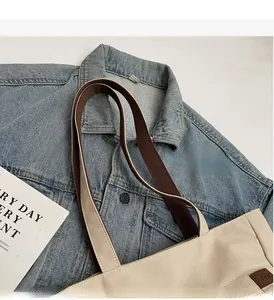 Detail of beige canvas tote bag showing dark brown straps and leather TENI brand patch
