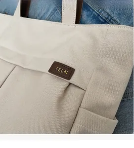 Close-up of cream canvas tote bag with brown leather brand tag on denim background