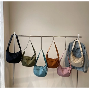 Six colors of nylon half-moon crossbody bags hanging on a rack with a denim jacket