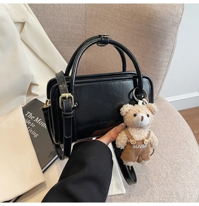 Close-up of black crossbody bag with gold hardware and a cute brown plush bear charm